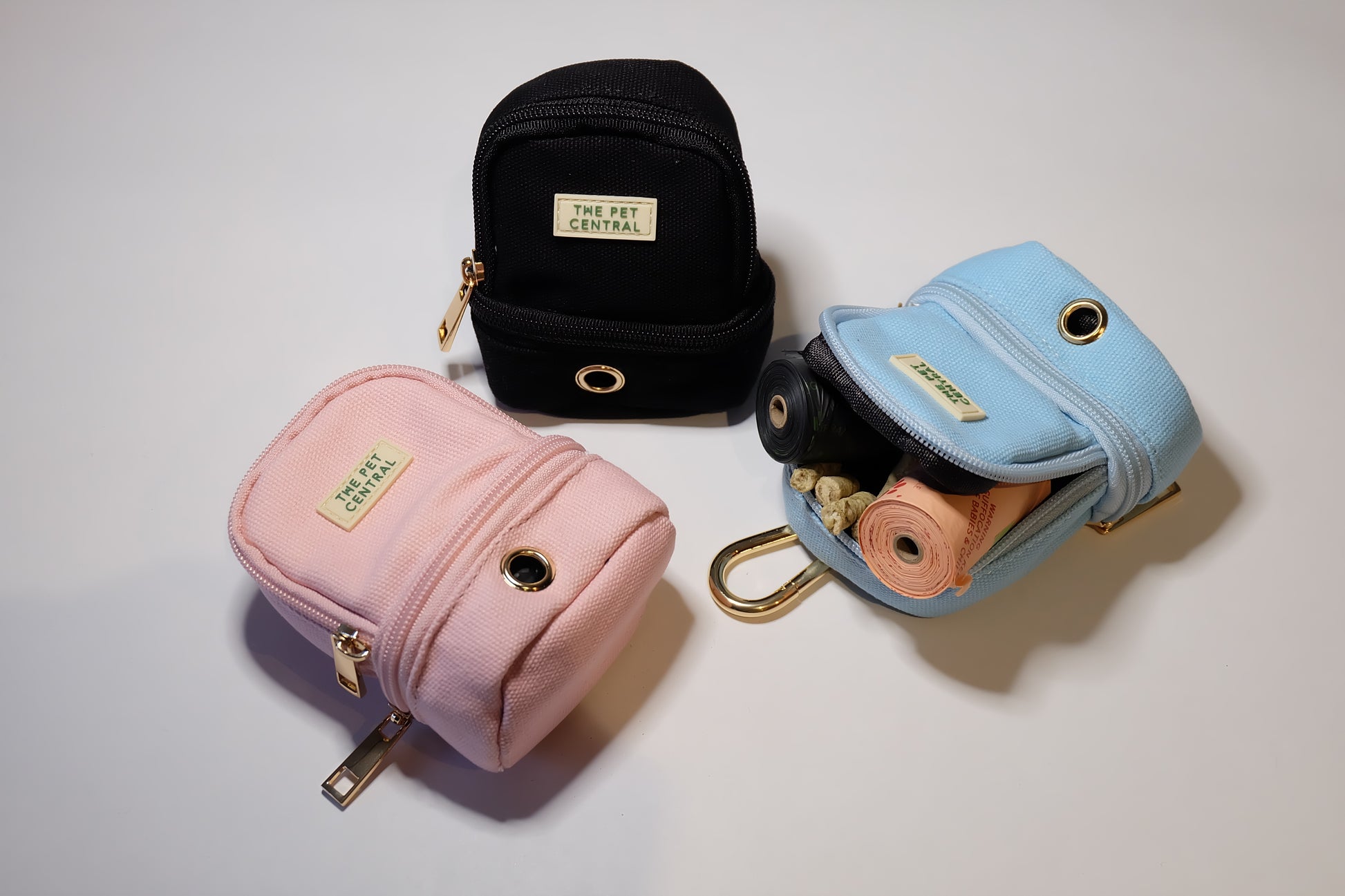 The Pet Central - The Paw Pack in Pink, Black, and Blue with an Open Compartment Showing Treats and Poop Bag Rolls